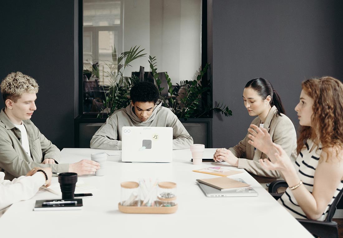 Diverse group of young professionals collaborating around a bright white conference table with a laptop, symbolizing teamwork, innovation, and strategic planning in a modern business environment.